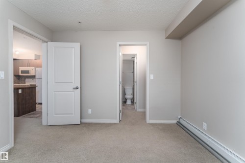 Neutral wall paint, textured ceiling, light-toned carpeting, white interior doors, and a baseboard heating unit - #202 105 Ambleside Dr Sw, Edmonton, AB 