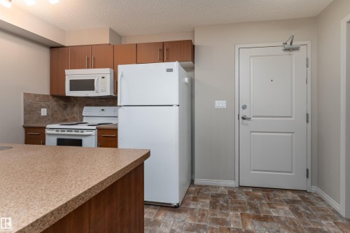 Kitchen featuring wood-finish cabinetry, white appliances, and a tiled backsplash - #202 105 Ambleside Dr Sw, Edmonton, AB 
