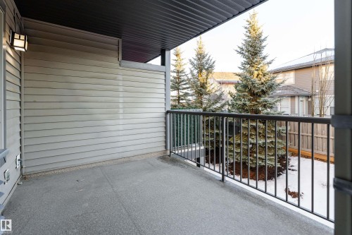 Covered outdoor patio with a concrete surface, black metal railing, and exterior wall sconce - #202 105 Ambleside Dr Sw, Edmonton, AB 