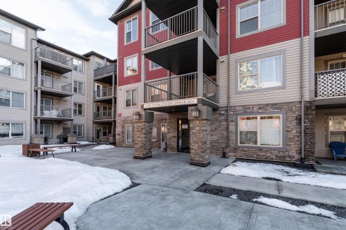 Stone facade entrance with exterior lighting, concrete walkway, and multiple residential balconies - #202 105 Ambleside Dr Sw, Edmonton, AB 