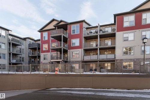 Multi-story building featuring balconies with metal railings, a stone-accented facade, and a combination of red and beige siding - #202 105 Ambleside Dr Sw, Edmonton, AB 