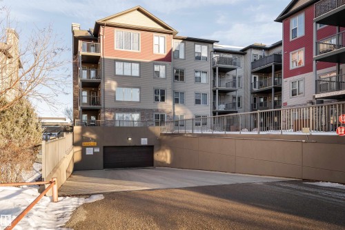 Multilevel building exterior featuring a mix of siding and stone veneer, multiple private balconies, and an integrated underground parking garage with ramp access - #202 105 Ambleside Dr Sw, Edmonton, AB 