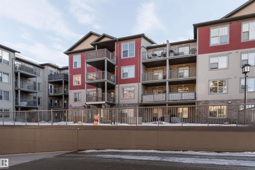 Multi-level residential building featuring exterior balconies, stone-finish siding, and a metal perimeter fence - #403 105 Ambleside Dr Sw, Edmonton, AB 