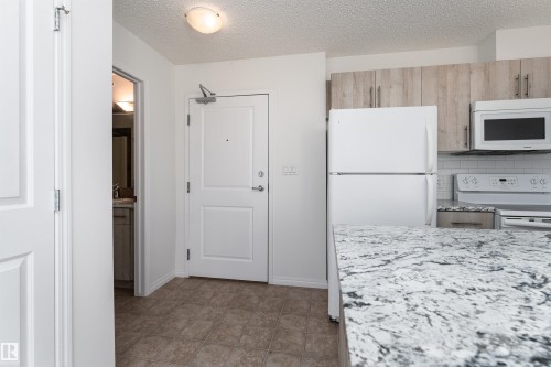 Kitchen featuring white appliances, a white subway tile backsplash, light wood-finish cabinetry, and a light-toned patterned countertop - #403 105 Ambleside Dr Sw, Edmonton, AB 