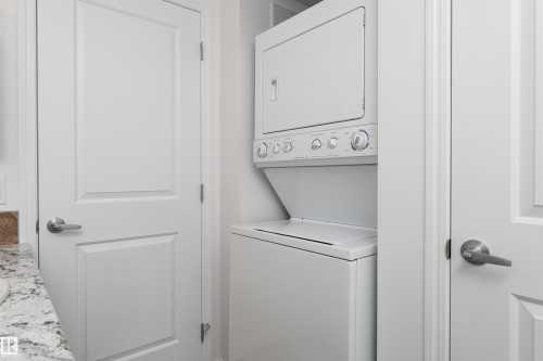 Stacked white washer and dryer units, white interior doors with satin nickel hardware, and a granite-patterned countertop - #403 105 Ambleside Dr Sw, Edmonton, AB 