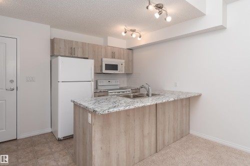 Kitchen featuring wood-finish cabinetry, white appliances, a double basin sink, and track lighting - #403 105 Ambleside Dr Sw, Edmonton, AB 