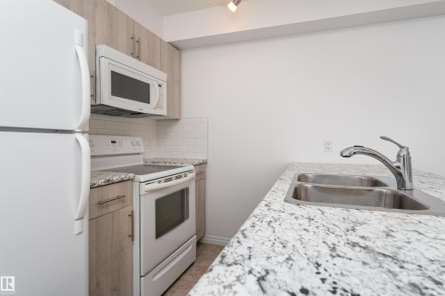 Light wood-finish cabinetry with silver hardware, white subway tile backsplash, white appliances, and speckled countertops - #403 105 Ambleside Dr Sw, Edmonton, AB 