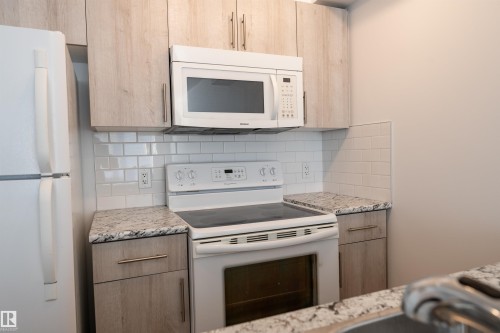 Wood-finish cabinetry paired with light-toned countertops and a white subway tile backsplash - #403 105 Ambleside Dr Sw, Edmonton, AB 