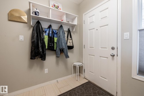 Entryway featuring a white paneled door with hardware, neutral tile flooring, and white wall-mounted built-in shelving with integrated hooks - 2093 Chalmers Way Sw, Edmonton, AB 