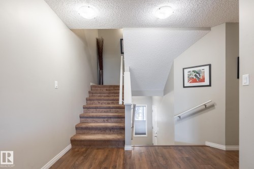 Staircase featuring wood-finish flooring, carpeted stairs, a white handrail, and dual flush-mount ceiling light fixtures - 2093 Chalmers Way Sw, Edmonton, AB 
