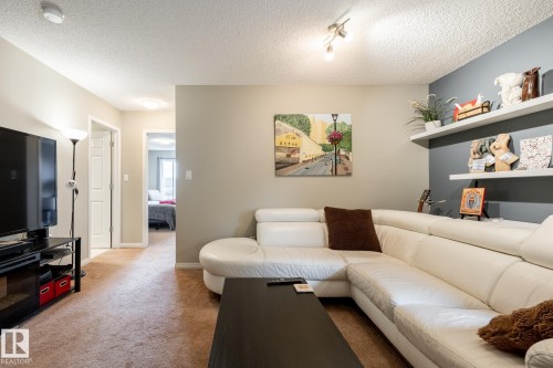 Living area featuring dual built-in wall shelving, an accent wall, multi-directional overhead track lighting, and neutral carpeting - 2093 Chalmers Way Sw, Edmonton, AB 
