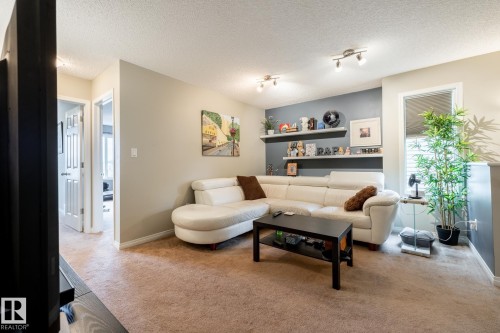 Living area featuring neutral wall tones, an accent wall with two built-in floating shelves, and dual track lighting fixtures - 2093 Chalmers Way Sw, Edmonton, AB 
