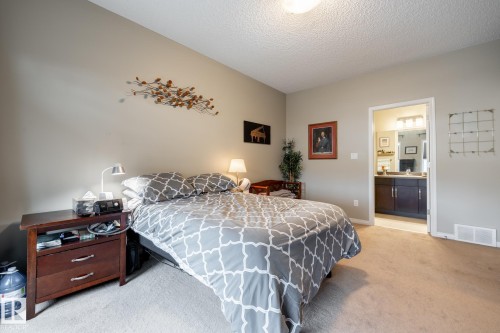 Room featuring neutral wall paint, carpeted flooring, and a flush-mount ceiling light fixture, with a doorway leading to a space containing a dark-toned vanity cabinet, countertop, and multi-bulb vanity light - 2093 Chalmers Way Sw, Edmonton, AB 