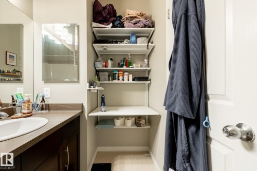 Bathroom featuring an oval drop-in sink, solid surface countertop, dark finish cabinetry with metal hardware, wall-mounted mirror, and adjustable white shelving system - 2093 Chalmers Way Sw, Edmonton, AB 
