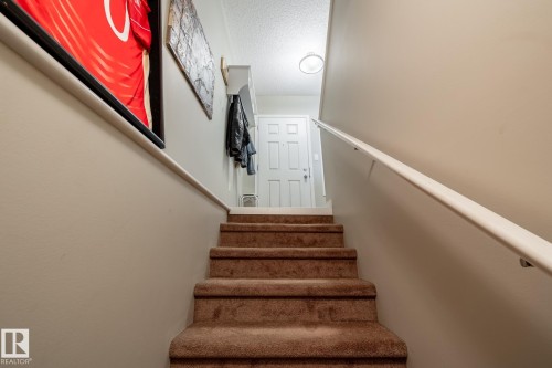 Staircase featuring wall-to-wall carpeting, a smooth-finish white handrail, a built-in wall-mounted coat rack with shelving, and a six-panel exterior entry door - 2093 Chalmers Way Sw, Edmonton, AB 