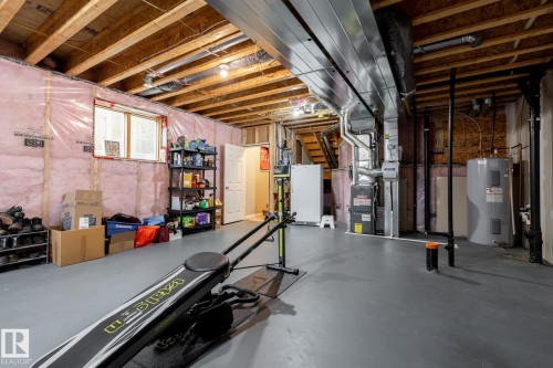 Unfinished lower level featuring exposed ceiling joists, painted concrete flooring, an installed water heater, and a high-efficiency furnace - 2093 Chalmers Way Sw, Edmonton, AB 