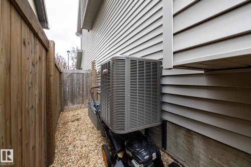 Exterior view featuring light-toned horizontal siding, central air conditioning unit, gravel ground cover, and a wood privacy fence with an integrated gate - 2093 Chalmers Way Sw, Edmonton, AB 
