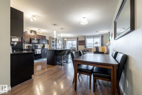 Kitchen featuring dark cabinetry, stone-finish countertops, a central island with pendant lighting, and wood-finish flooring - 2093 Chalmers Way Sw, Edmonton, AB 