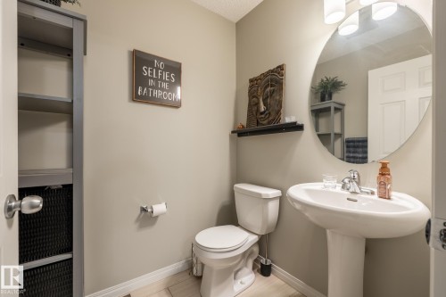 Bathroom featuring a pedestal sink, oval wall-mounted mirror, three-light vanity fixture, and built-in shelving unit - 2093 Chalmers Way Sw, Edmonton, AB 