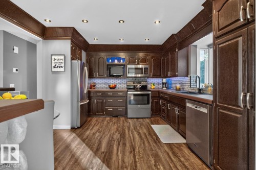 Wood-finish flooring, recessed lighting, dark wood cabinetry, white tile backsplash, and stainless steel appliances - 5502 48 Avenue, Beaumont, AB 