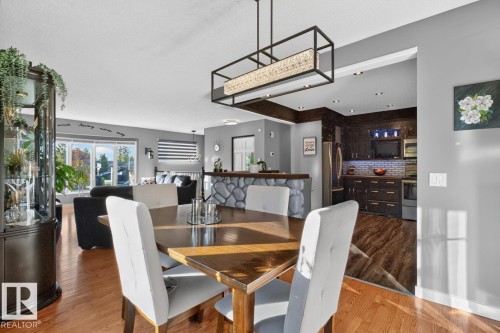 Hardwood flooring, contemporary linear chandelier, rock-finish breakfast bar, dark wood-finish cabinetry, and bay window - 5502 48 Avenue, Beaumont, AB 