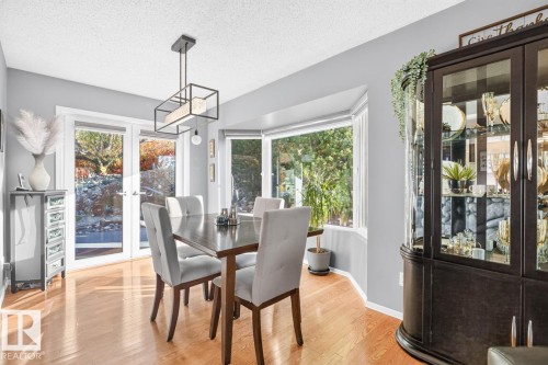 Light wood-finish flooring, a contemporary linear chandelier, and a built-in display cabinet - 5502 48 Avenue, Beaumont, AB 