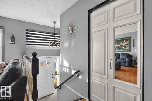 White paneled bifold doors with integrated mirrors, a white entry door with an arched window, and a black and white striped window treatment - 5502 48 Avenue, Beaumont, AB 
