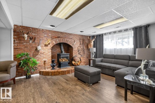 Exposed brick wall with an arched wood-burning fireplace and hearth, wood-finish flooring, and drop-panel ceiling with integrated lighting - 5502 48 Avenue, Beaumont, AB 