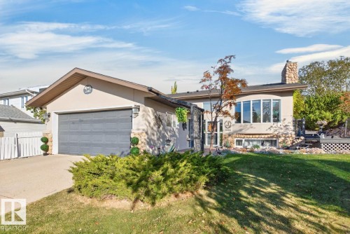 Stucco exterior with stone accents, attached garage, large bay windows, stone chimney, and a multi-level deck - 5502 48 Avenue, Beaumont, AB 
