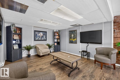 Wood-finish flooring, exposed brick wall feature, drop ceiling with recessed lighting panels, and built-in shelving units - 5502 48 Avenue, Beaumont, AB 