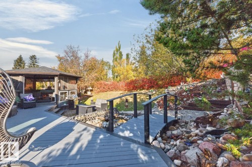 Expansive tiered decking with a built-in screened gazebo, stone-lined landscaping, a decorative bridge, and mature trees - 5502 48 Avenue, Beaumont, AB 