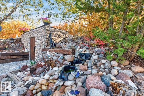 Stone-clad outbuilding with a wood door, surrounded by a rock garden with a water feature and mature trees - 5502 48 Avenue, Beaumont, AB 