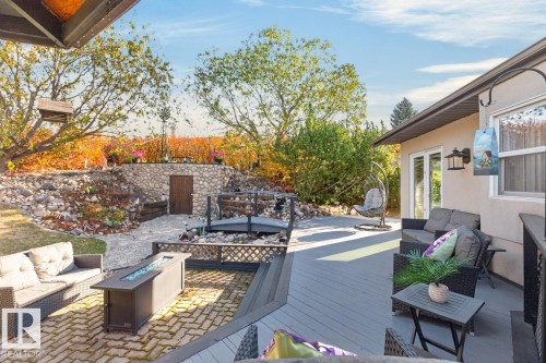 Multi-level deck with a built-in fire pit, stone-clad retaining wall, and a bridge feature over a water element - 5502 48 Avenue, Beaumont, AB 
