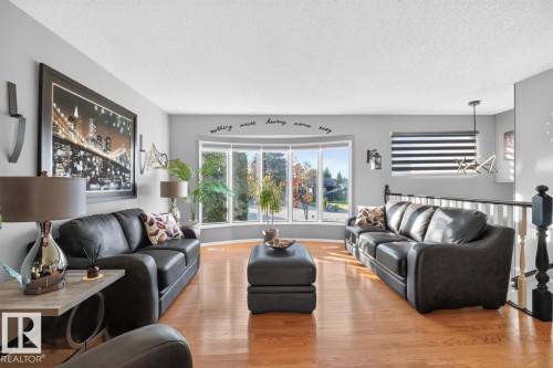 Hardwood flooring throughout, a bay window with multiple panes, a modern pendant light fixture, and a white and black staircase railing - 5502 48 Avenue, Beaumont, AB 