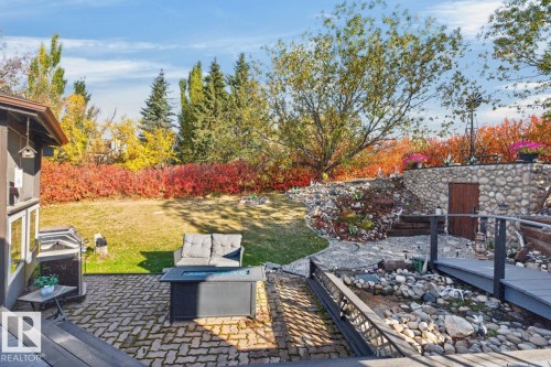 Paver patio with a fire pit, tiered landscaping featuring a stone retaining wall, and a multi-level garden - 5502 48 Avenue, Beaumont, AB 