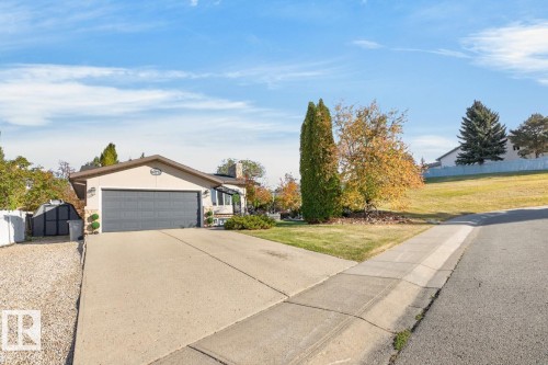 Exterior featuring a paved driveway, attached garage, and a sloped, grassed yard - 5502 48 Avenue, Beaumont, AB 