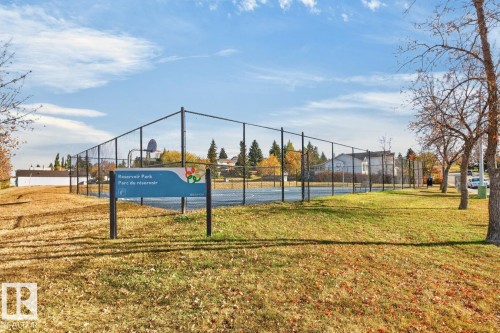 Chain-link fenced court with a basketball hoop, surrounded by a grassy area with mature trees - 5502 48 Avenue, Beaumont, AB 
