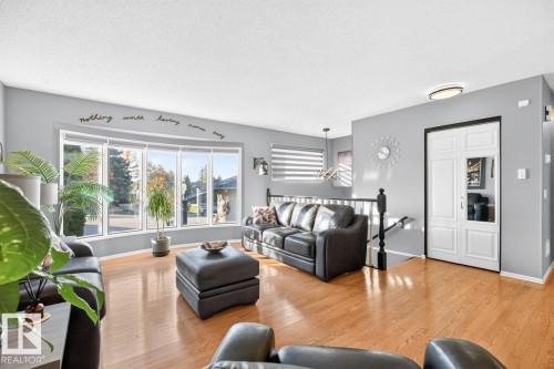 Bay window with multiple panes, hardwood-finish flooring, two-panel bifold door with mirrored inserts, and a black-finished staircase railing - 5502 48 Avenue, Beaumont, AB 