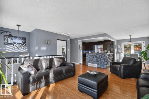 Hardwood flooring, painted interior walls, contemporary ceiling light fixture, stone-clad breakfast bar, and white balustrade - 5502 48 Avenue, Beaumont, AB 