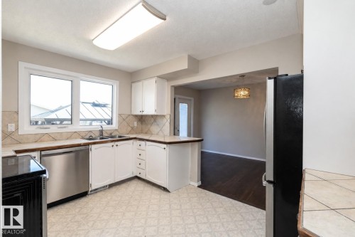 Kitchen featuring white cabinetry, stainless steel dishwasher, dual basin sink, and mosaic tile backsplash - 17311 107 Street Nw, Edmonton, AB 