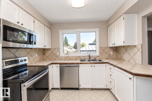 White cabinetry with dark pulls, stainless steel appliances, tile countertops, and a tile backsplash with a diamond pattern - 17311 107 Street Nw, Edmonton, AB 