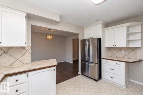 White cabinetry with dark hardware, stainless steel refrigerator, tile countertops, tile backsplash, and patterned flooring - 17311 107 Street Nw, Edmonton, AB 