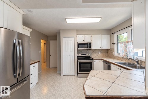 Stainless steel appliances, white cabinetry, tile countertops, tile backsplash, and a double basin sink - 17311 107 Street Nw, Edmonton, AB 