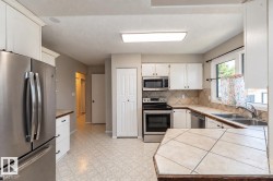 Stainless steel appliances, white cabinetry, tile countertops, tile backsplash, and a double basin sink - 