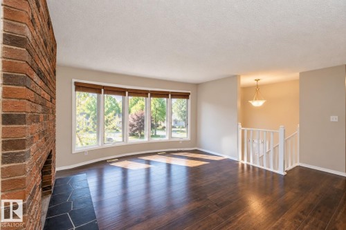 Spacious living area featuring wood-finish flooring, a brick fireplace with a stone hearth, and a bay window with natural light - 17311 107 Street Nw, Edmonton, AB 