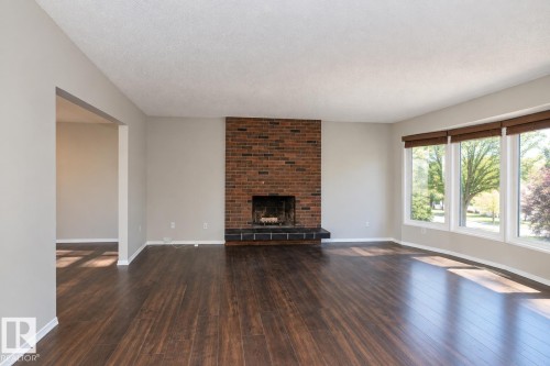 Spacious living area featuring wood-finish flooring, a brick-surround fireplace, and a large bay window with natural light - 17311 107 Street Nw, Edmonton, AB 