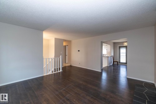 Wood-finish flooring, white wall paint, open archway, staircase with white railing, and a rear door with integrated blinds - 17311 107 Street Nw, Edmonton, AB 