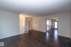 Wood-finish flooring, white wall paint, open archway, staircase with white railing, and a rear door with integrated blinds - 
