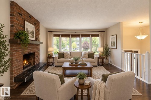 Living area featuring a brick fireplace with a wood mantle, a tiled hearth, wood-finish flooring, and a bay window - 17311 107 Street Nw, Edmonton, AB 
