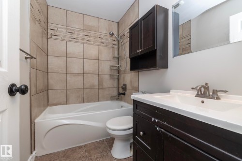 Full bathroom featuring a white tub, coordinating toilet, and a vanity with an integrated sink and brushed nickel faucet - 17311 107 Street Nw, Edmonton, AB 